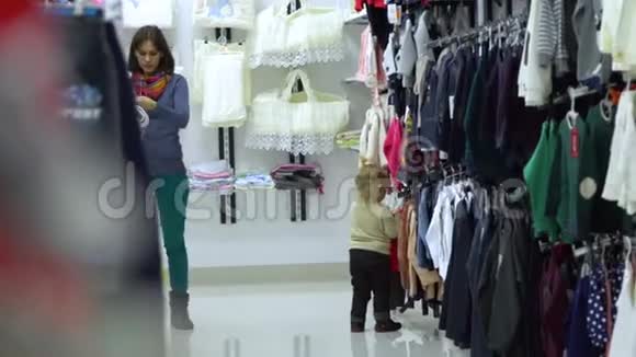 一个可爱的小女孩和她的母亲在一家精品店里家精品店妈妈和孩子在商店里选择衣服视频的预览图