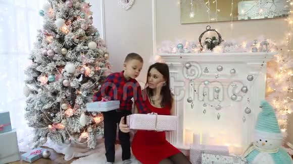 快乐的母亲和小儿子正在看新年的礼物节日的内部视频的预览图
