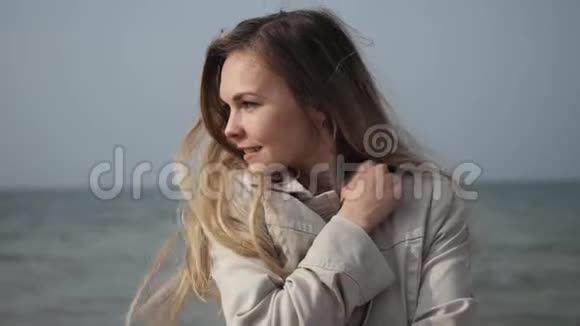 年轻快乐的女人长发穿着米色外套特写在海边跳舞视频的预览图