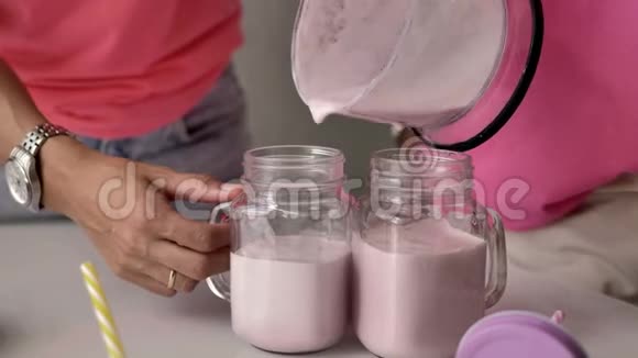 女性的手把粉红色奶昔倒入透明的玻璃杯中视频的预览图