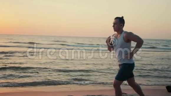 运动员在日落时沿着海岸跑步在沙滩上打电话视频的预览图