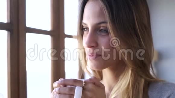 美丽的年轻女子站在窗户附近在家里的客厅喝咖啡视频的预览图