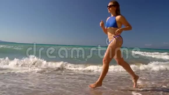海滩比基尼女郎无忧无虑地沿着海滩上的水奔跑希腊科孚海岸风景如画慢动作视频的预览图