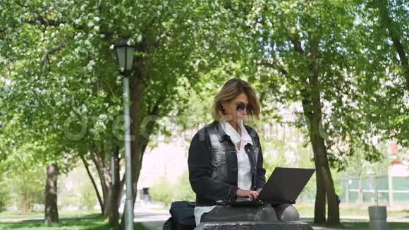 坐在公园长凳上用笔记本电脑的女人视频的预览图