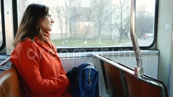 穿着橙色外套背着蓝色袋子的可爱女孩乘坐公共交通工具布鲁内特透过电车窗和视频的预览图