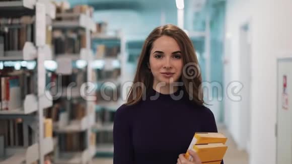 留着长发的女孩直视着摄像机沿着图书馆的书架走着视频的预览图