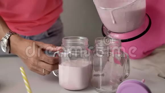 女性的手把粉红色奶昔倒入透明的玻璃杯中视频的预览图