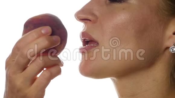 美丽的女人在白色的背景上吃桃子特写女孩咬桃子慢动作视频的预览图