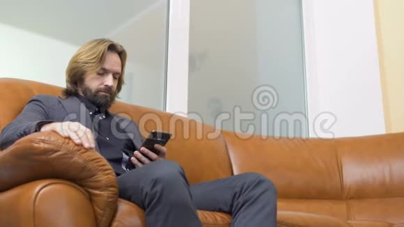 帅哥商人坐在沙发上用电话视频的预览图