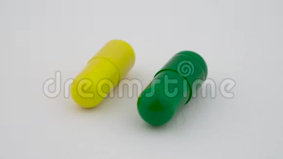 两个硬淀粉胶囊旋转在转盘上黄色和绿色孤立在白色背景上关门视频的预览图