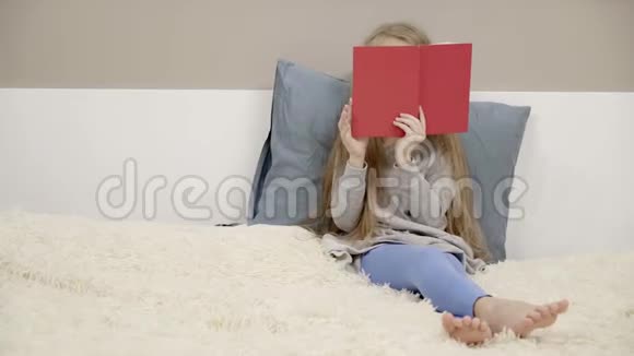 穿着连衣裙和紧身裤的小女孩坐在床上看书视频的预览图
