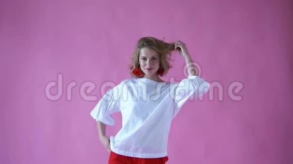 在一个粉色背景的摄影棚里一个开朗积极向上的金发女孩在为照相机摆姿势视频的预览图