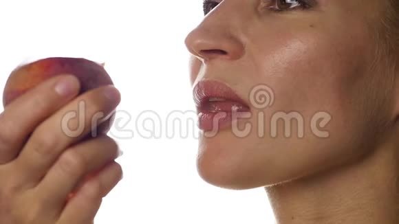 美丽的女人在白色的背景上吃桃子特写女孩咬桃子慢动作视频的预览图