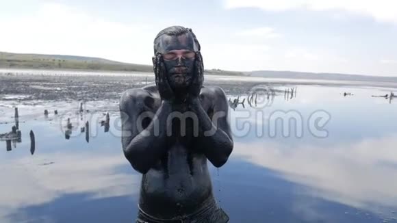 在盐水湖上用黑色医用泥浆做面罩的年轻人咸黑的衣服对有视频的预览图