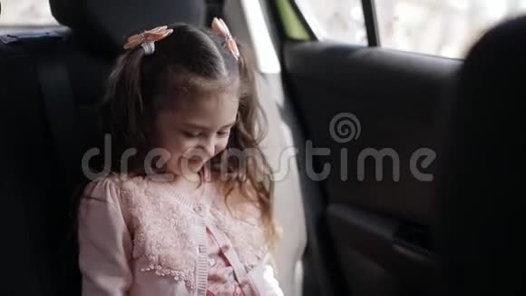 漂亮的蓝眼睛小女孩坐在后座的车里她把游戏集中在电话上视频的预览图