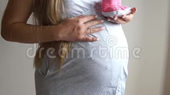 孕妇抱着婴儿靴怀孕的女孩女人摸她怀孕的肚子视频的预览图