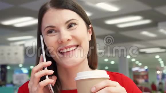 在食品场的快餐店里一个口渴的女孩从纸杯里喝咖啡在电话里说话视频的预览图