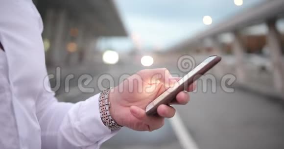 在工作的商人穿着白衬衫手臂丰美的年轻人在智能手机上输入了数字视频的预览图