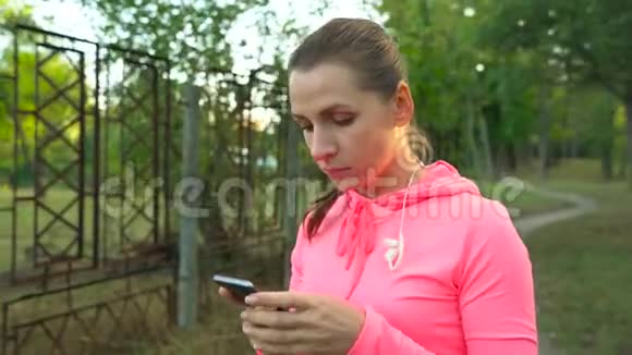 带着无线耳机和智能手机的女人选择音乐穿过秋天公园视频的预览图