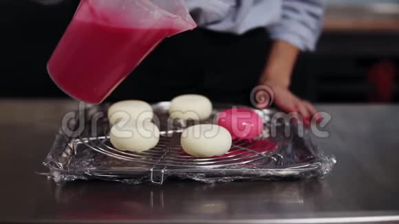 特写镜头女糖果在准备好的白色饼干上倒入粉红色的镜子釉在锅上正面观点视频的预览图