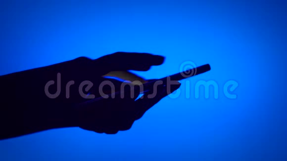 黑色轮廓女性手影使用智能手机触摸屏上的蓝色背景打字信息视频的预览图