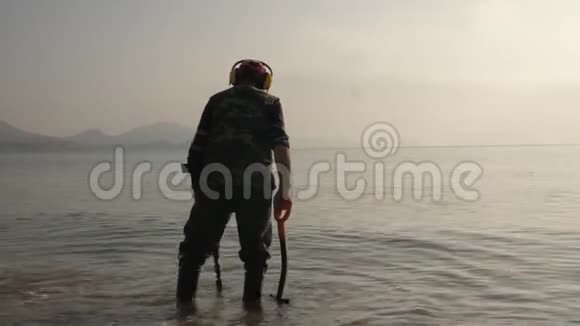一个带着金属探测器的人正在海滩上寻找贵重物品视频的预览图