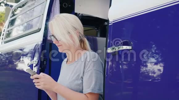 一个女人正在使用智能手机在紫罗兰色复古车的台阶上视频的预览图