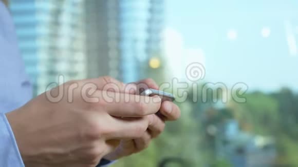 特写镜头男人的手在窗户的背景下使用电话从窗户上可以看到摩天大楼视频的预览图