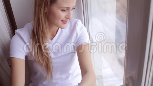 坐在窗台上的迷人梦想的年轻女子的画像视频的预览图