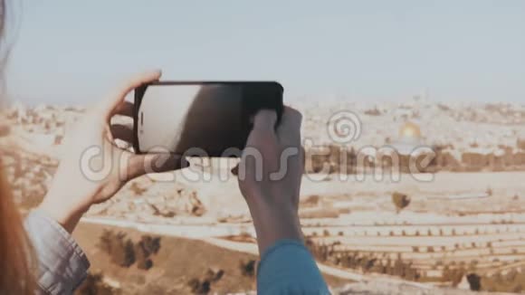 在阳光明媚的日子里女性手握智能手机捕捉瞬间女人拍耶路撒冷全景4K的电话照片视频的预览图