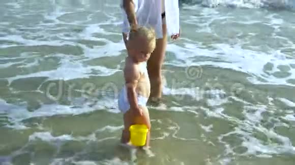 妈妈和小女儿正在海滩上散步妈妈牵着女儿手那个女孩拿着一个玩具桶这就是视频的预览图