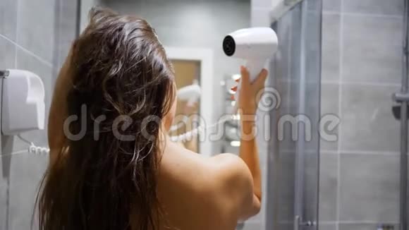年轻女性在镜子前的浴室里用吹风机吹湿头发视频的预览图
