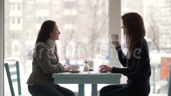 两个女朋友坐在餐桌旁在自助餐厅喝着杯子里的咖啡视频的预览图