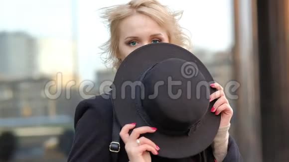 穿着黑色外套的贴身漂亮女孩戴着帽子带着耳机听音乐对抗模糊的现代建筑慢动作视频的预览图