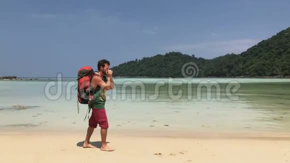 徒步旅行者快乐背着旅游背包在温暖的海水蔚蓝的热带海岸边走着一边竖着竖琴演奏视频的预览图