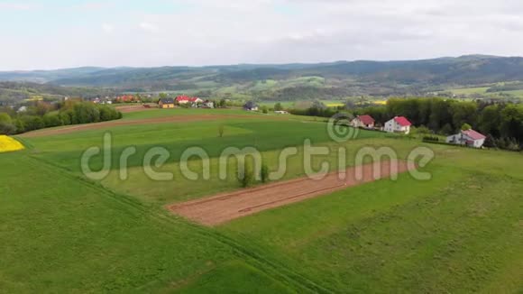 在一个有小房子的村庄里鸟瞰绿色的田野山丘和树木波兰视频的预览图