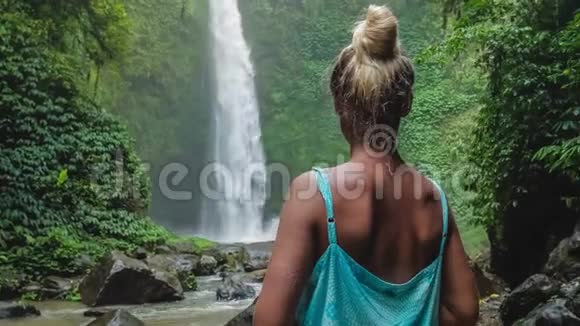 女人在热带瀑布前被郁郁葱葱的绿色丛林包围落水撞击水面轻微的风视频的预览图