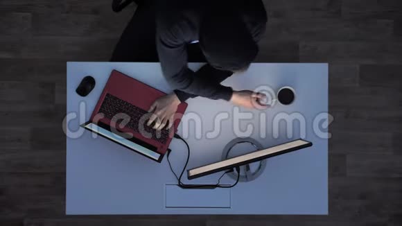 穿着黑色连帽衫的年轻人在晚上喝着咖啡在笔记本电脑上打字坐在白色的桌子后面拍得好视频的预览图