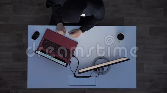 穿着黑帽衫的年轻人伸着手指在笔记本电脑上打字晚上看着显示器坐在后面视频的预览图