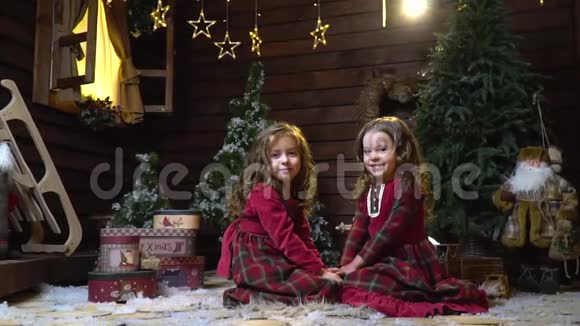 两个穿着连衣裙的小女孩正坐在房间的中间上面摆着新年装饰周围有礼物视频的预览图