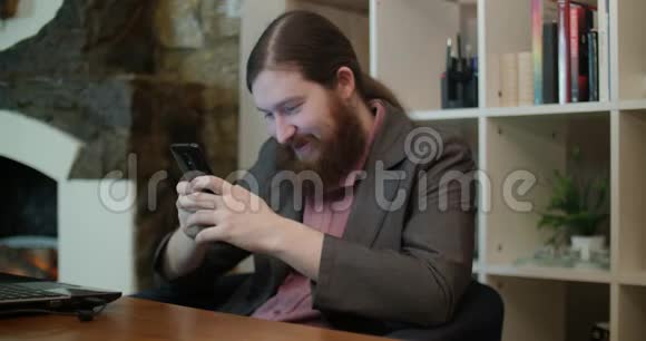有胡子的非正式男人在办公室里用智能手机视频的预览图