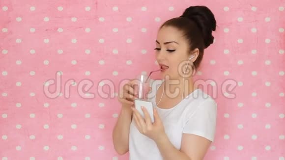 年轻女子用吸管喝着浆果冰沙微笑着看着他的智能手机屏幕女孩用的是视频的预览图