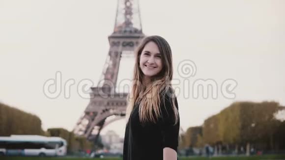 年轻快乐的女人站在法国巴黎的埃菲尔铁塔附近微笑着看着相机发送着吹吻视频的预览图