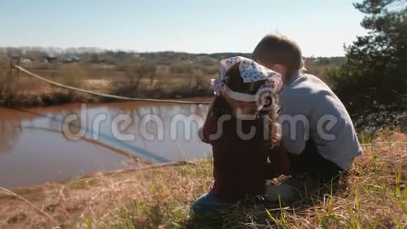 兄妹俩坐在村里的河岸上玩耍后景视频的预览图