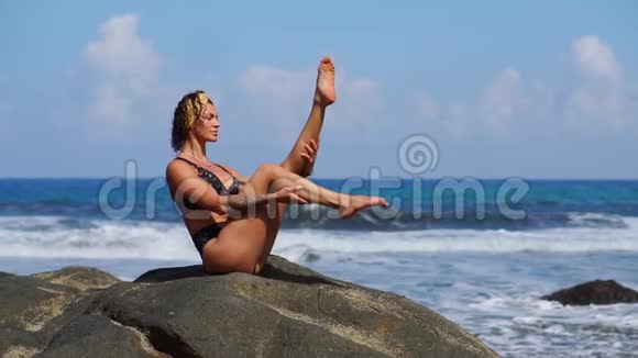 在海滩上健身的女人穿着泳衣坐在熔岩山周围的岩石上穿着火山黑沙视频的预览图