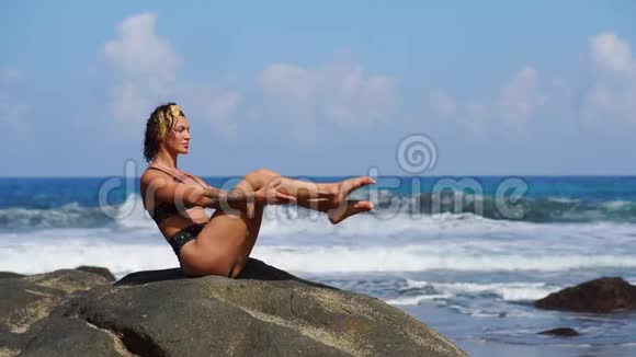 在海滩上健身的女人穿着泳衣坐在熔岩山周围的岩石上穿着火山黑沙视频的预览图