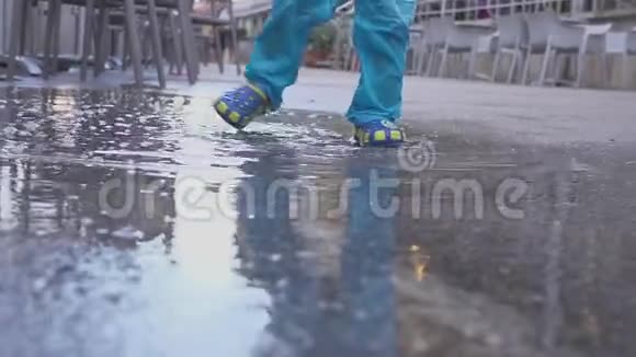 这个男孩在雨中的水坑里玩他在雨中快乐两岁的男孩在人行道上奔跑概念视频的预览图
