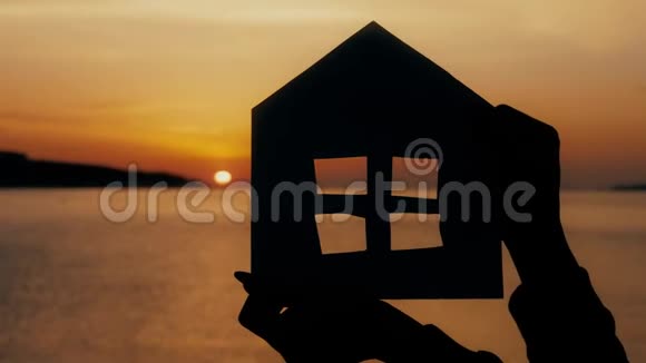 剪影一个用纸板做的小纸屋在海上日落时用手握住效率及家居概念视频的预览图