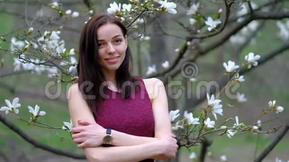 初春时年轻漂亮的苗条女子在盛开的木兰树和花朵上摆姿慢悠悠视频的预览图