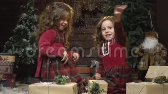 两个穿着红裙子的女孩在礼物和新年装饰中玩得很开心而正在下雪很慢视频的预览图